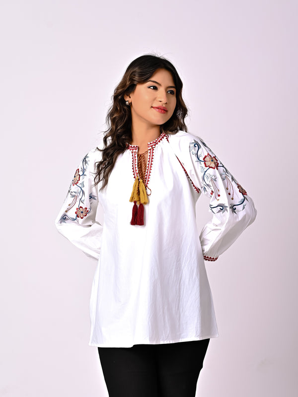 Woman wearing a white blouse with colorful embroidery on a plain background